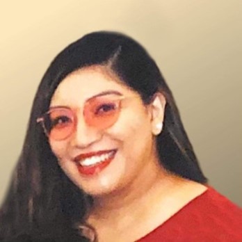 A Latina Women with black, long hair wearing red glasses and wearing a red shirt smiling