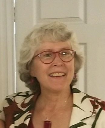 A white woman with white shoulder length hair with maroon glasses