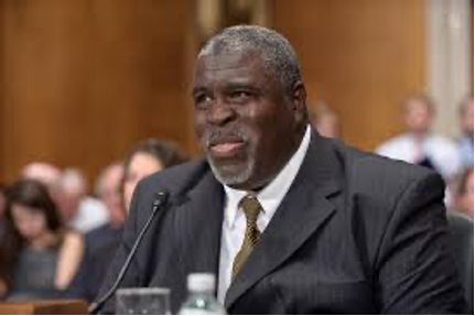 An African American man with a beard and gray hair in a suit testifies 