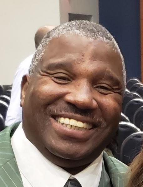 A African American man with a kind smile, grey hair, and a green suit